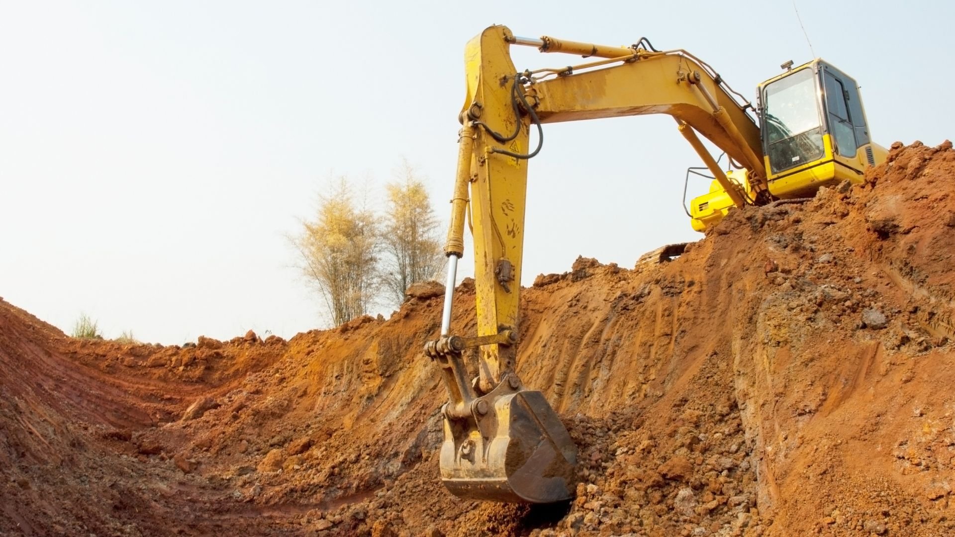 Yellow excavator digging earth on construction site with trees in background