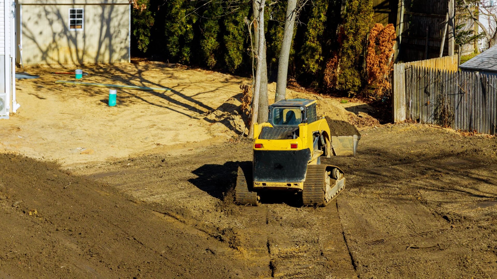 Yellow tracked skid steer excavating dirt in residential backyard