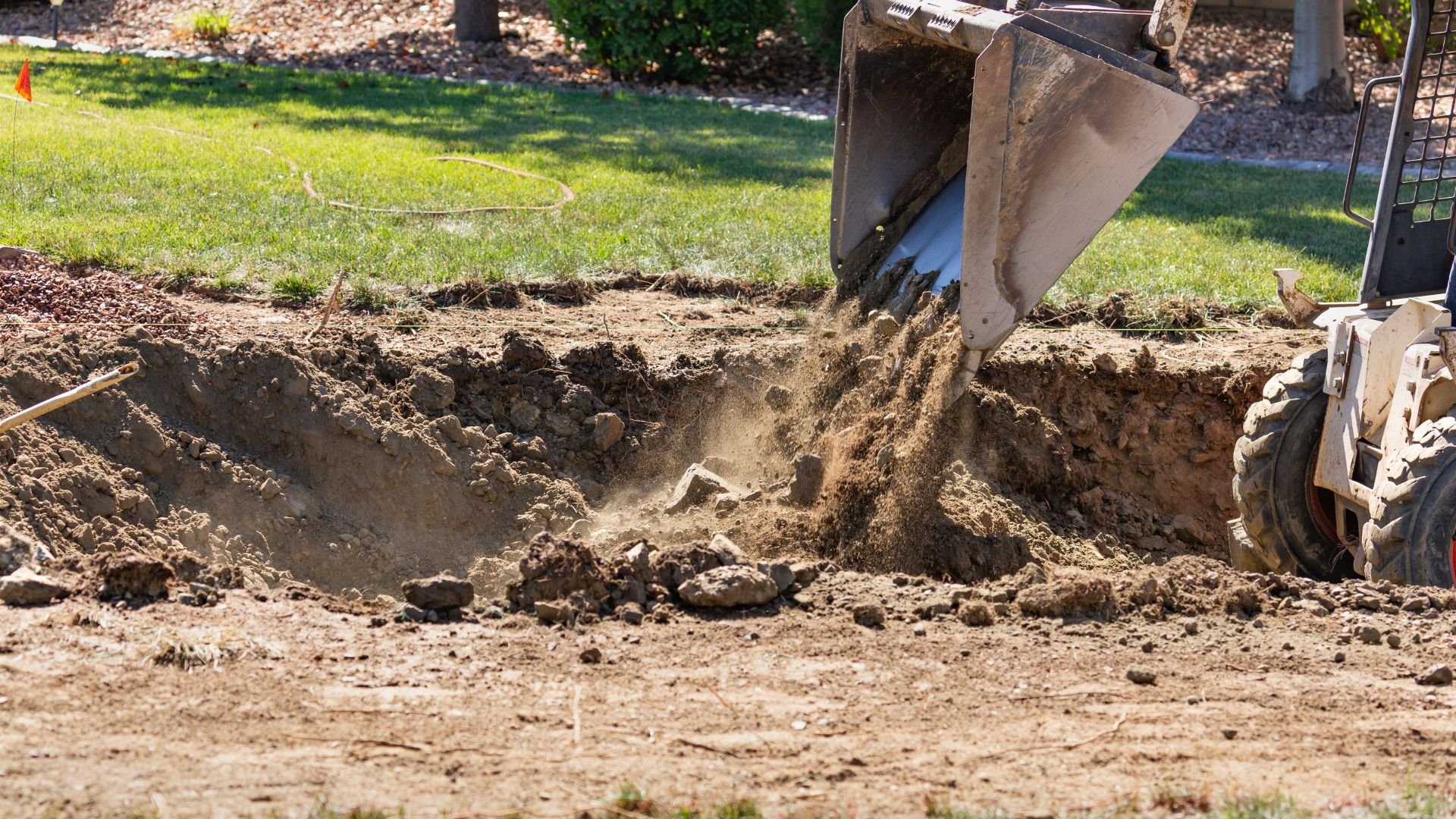 Excavator digging large hole in grassy backyard landscaping area